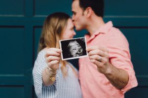 Photo by Kelly Sikkema man kissing woman's forehead white holding ultrasound photo